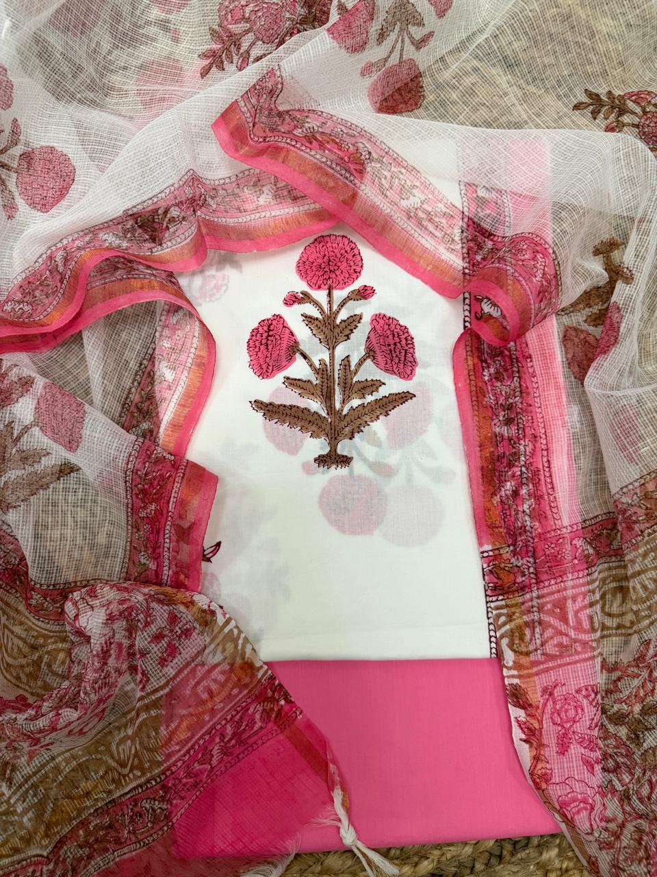 Overhead flatlay of white cotton Mughal block print kurta panel – pink marigold floral motif with brown stem, paired with solid pink bottom fabric and sheer Kota Doria dupatta with pink floral border, unstitched 3-piece suit set