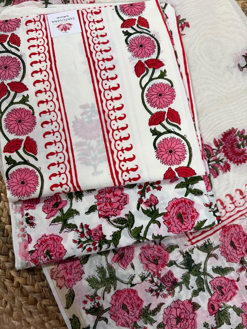 Straight flatlay of white cotton placement floral block print unstitched kurta – pink dahlia and red tulip vine border strip with red scallop edge, folded with Tantuvana tag, pink rose and green leaf bottom fabric below and sheer Chanderi dupatta partially visible 