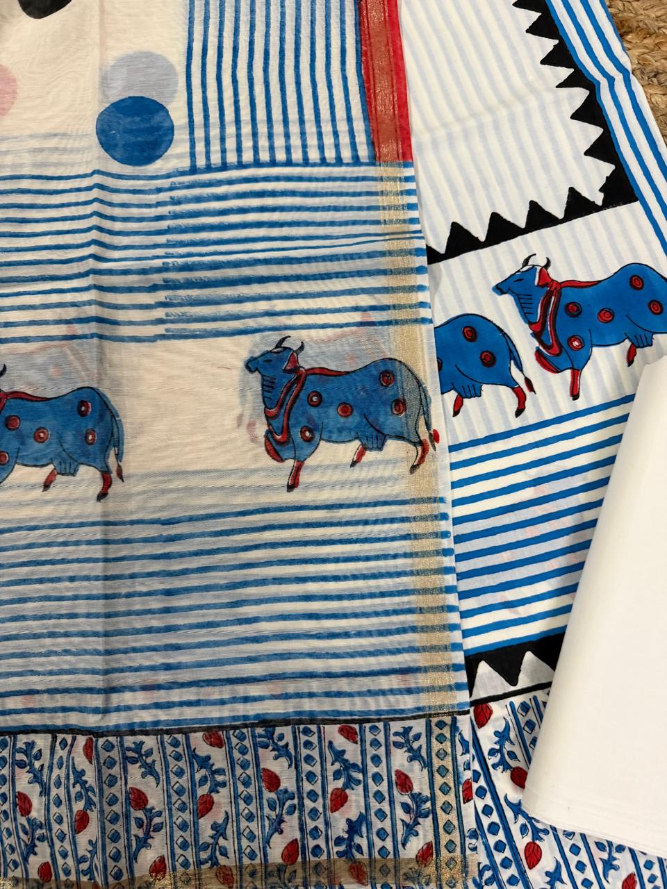 Straight close-up of white cotton Pichwai placement block print kurta – blue decorated cow motifs on blue horizontal stripe body with black zigzag border, alongside sheer Chanderi dupatta with blue stripe and red border, cream bottom
