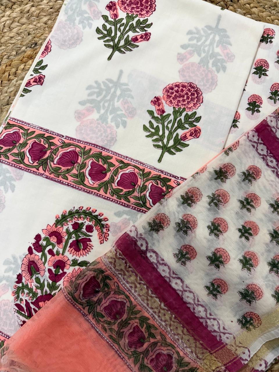 Angled flatlay of white cotton placement block print kurta fabric – scattered pink marigold butti with large paisley floral panel and pink floral border, paired with sheer Chanderi dupatta