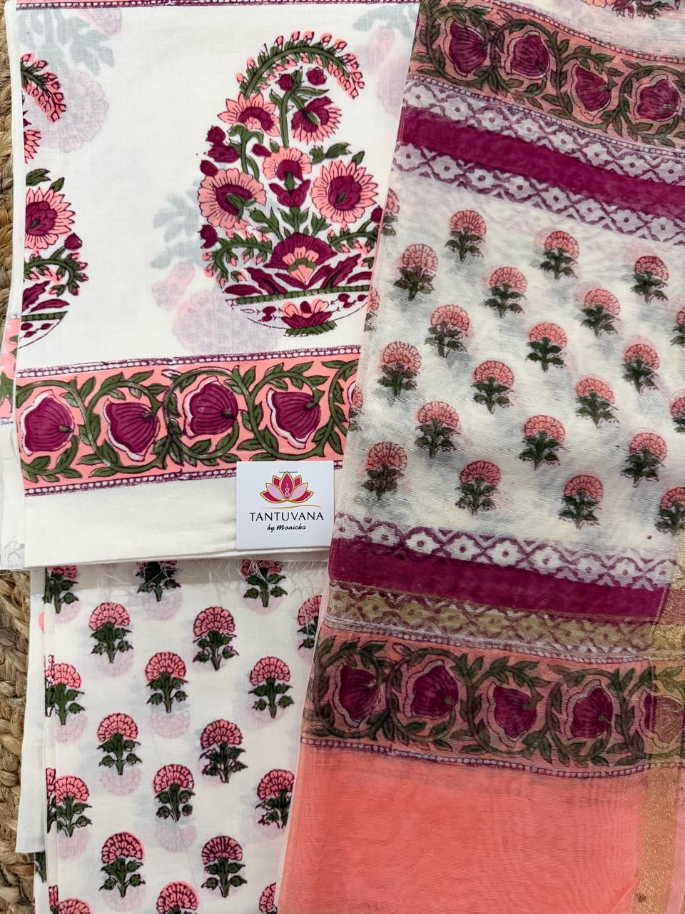 Angled flatlay of white cotton placement block print 3-piece unstitched suit set – paisley floral kurta panel with pink border, scattered marigold butti bottom and sheer Chanderi dupatta with floral border