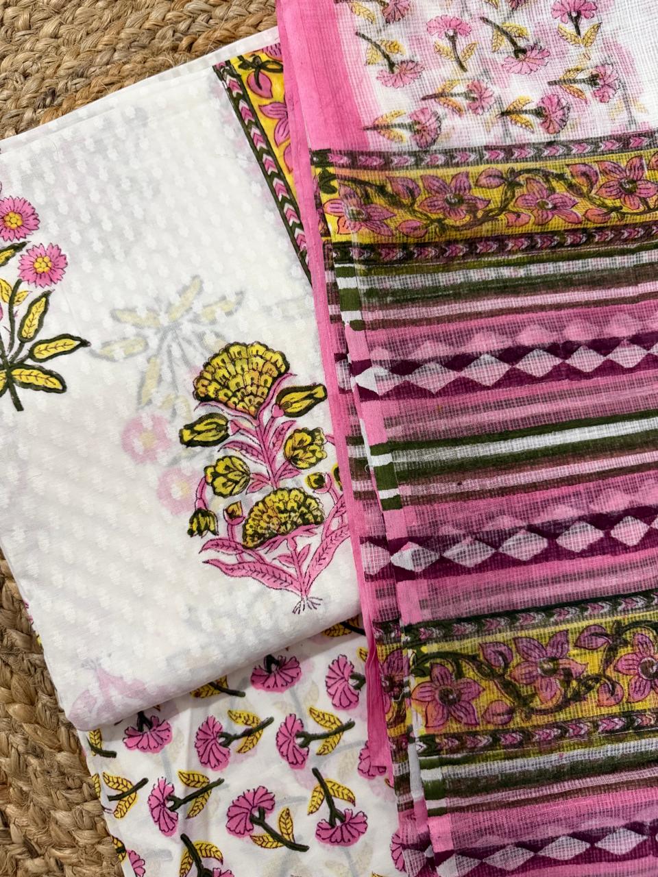 Angled flatlay of white cotton Mughal block print kurta – pink and yellow marigold floral butti with yellow floral vine border strip, alongside sheer Kota Doria dupatta with pink and olive stripe and diamond weave pattern