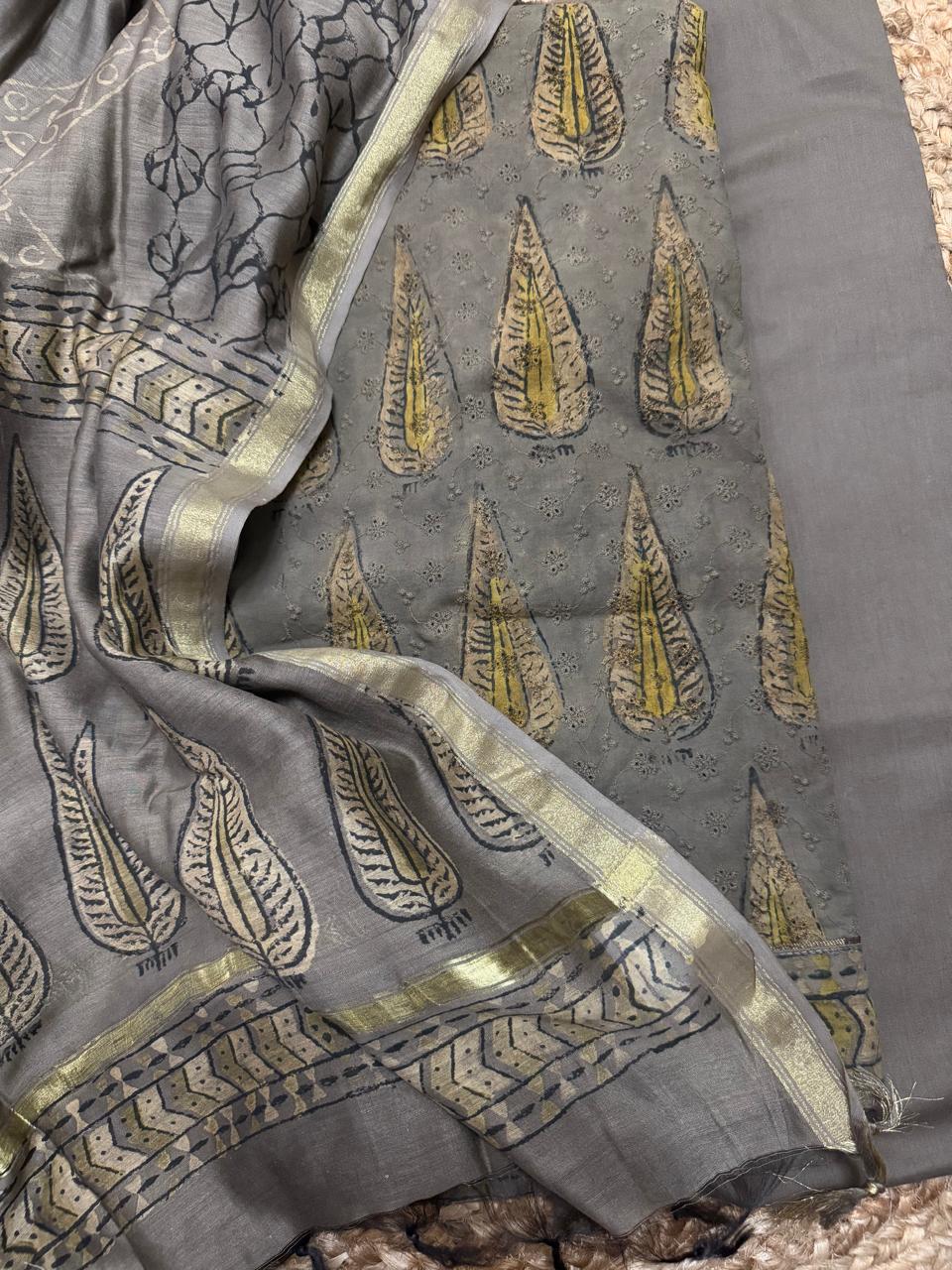 Overhead flat lay of grey Ajrakh cotton hakoba kurta set showing Ajrakh leaf block print fabric, hakoba embroidery panel, and Chanderi silk dupatta with zari border
