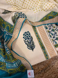 Close flat lay of cream cotton block print kurta fabric with teal-green floral bouquet block print motif, golden border with teal piping, alongside teal block print dupatta and cream polka dot fabric on jute mat 