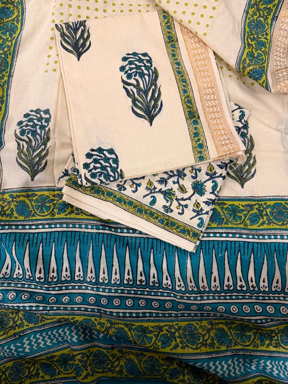 Full flat lay of cream cotton block print 3-piece unstitched suit set showing kurta fabric with teal-green floral bouquet motifs, folded bottom fabric with teal floral vine print border, and cream polka dot dupatta with teal block print border
