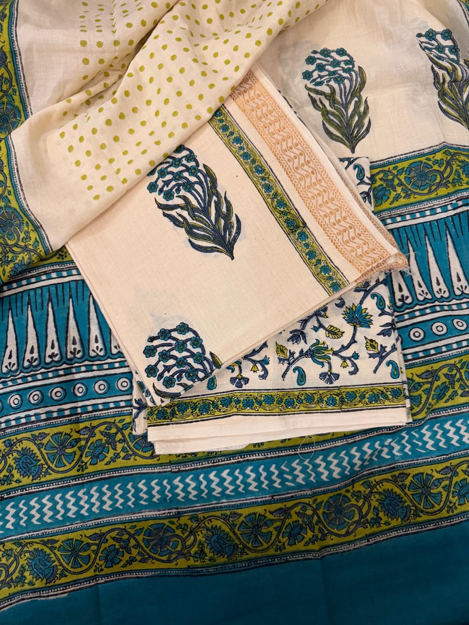 Flat lay of cream cotton block print 3-piece unstitched suit set showing kurta fabric with teal-green floral bouquet motif and golden border, cream floral vine bottom fabric, and cream polka dot dupatta, all layered over teal block print dupatta with green-yellow geometric border