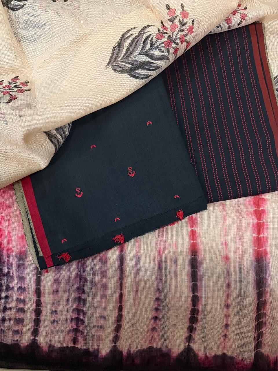 Styled flat lay of black handloom cotton kurta fabric with red anchor motifs, dark striped cotton bottom, and Kota Doria dupatta with shibori-dyed pink-red border and floral block print