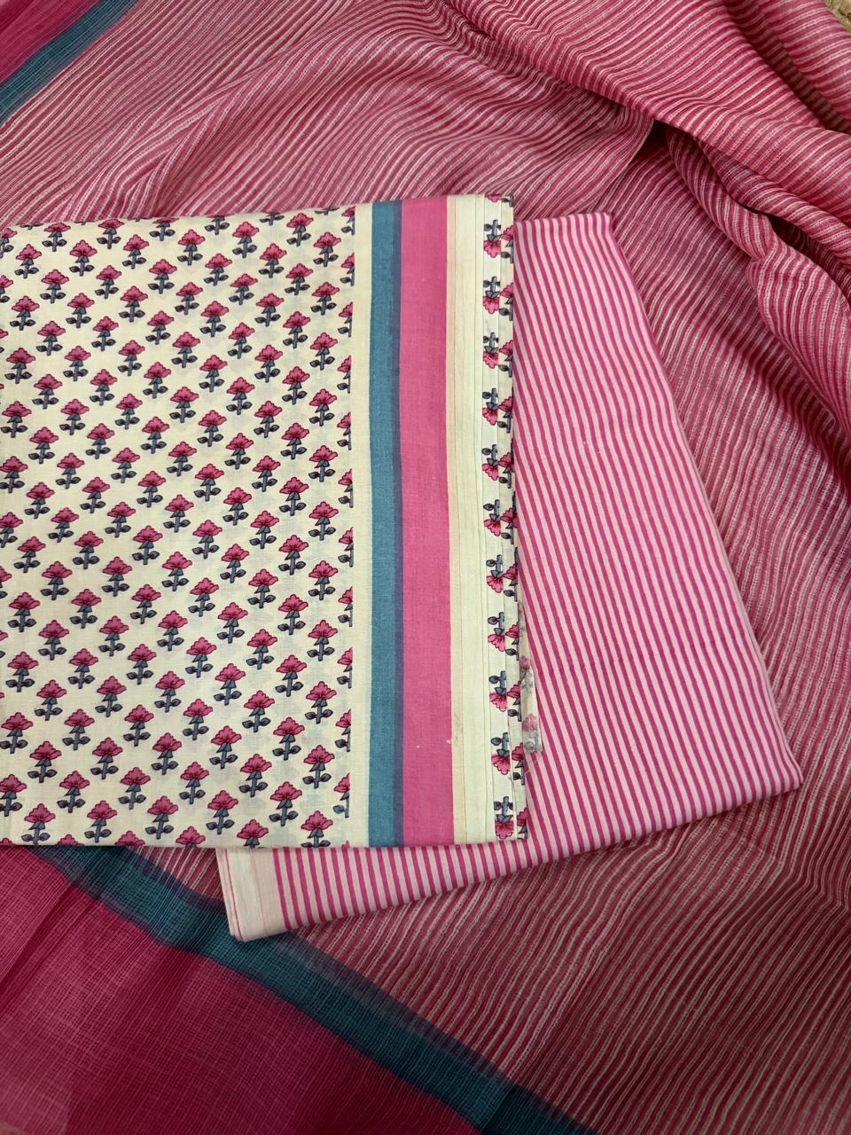 Flat lay of cream and pink cotton block print unstitched suit set with pink striped Kota Doria dupatta, showing all three fabric pieces — floral block print kurta, pink-blue striped border panel, and pink striped cotton bottom
