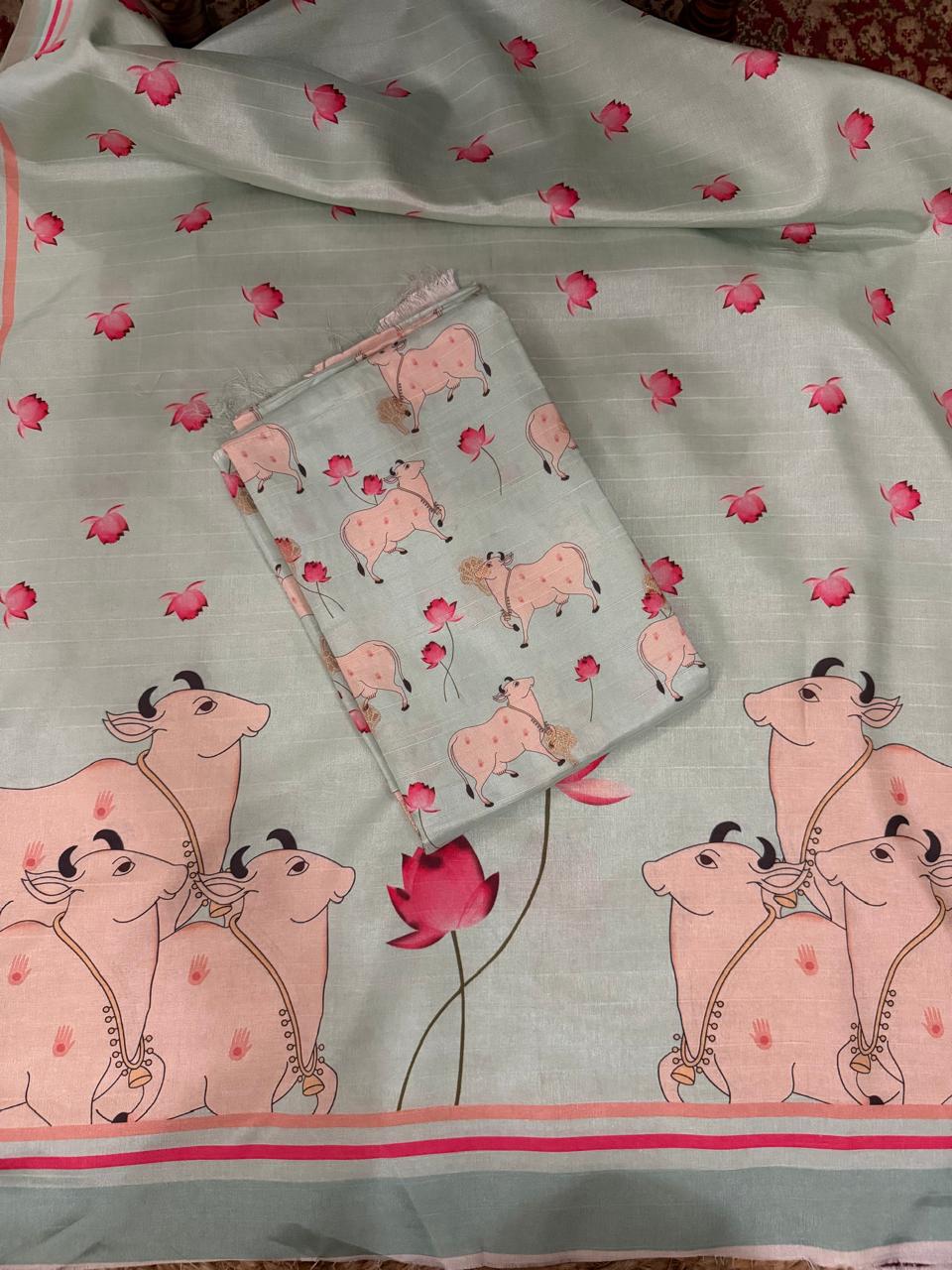 Overhead flat lay of powder green Banarasi semi tussar unstitched suit set showing folded Pichwai print kurta fabric with Kamadhenu cows and pink lotus motifs, placed over full kurta length with large Pichwai cow border at bottom