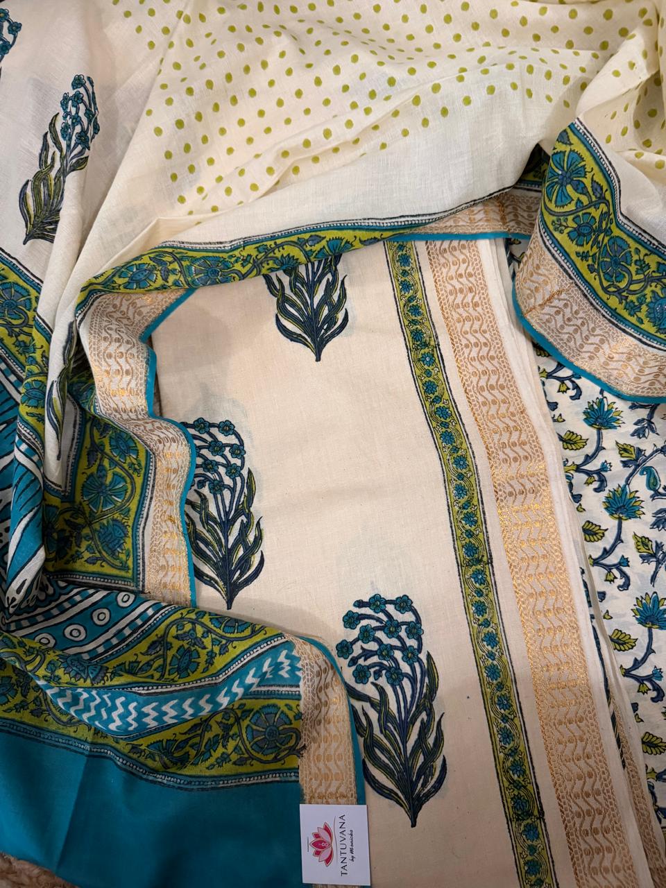 Flat lay of cream cotton block print unstitched kurta fabric with repeated teal-green floral bouquet motifs and golden border, alongside teal block print dupatta with green-yellow floral border and cream polka dot fabric