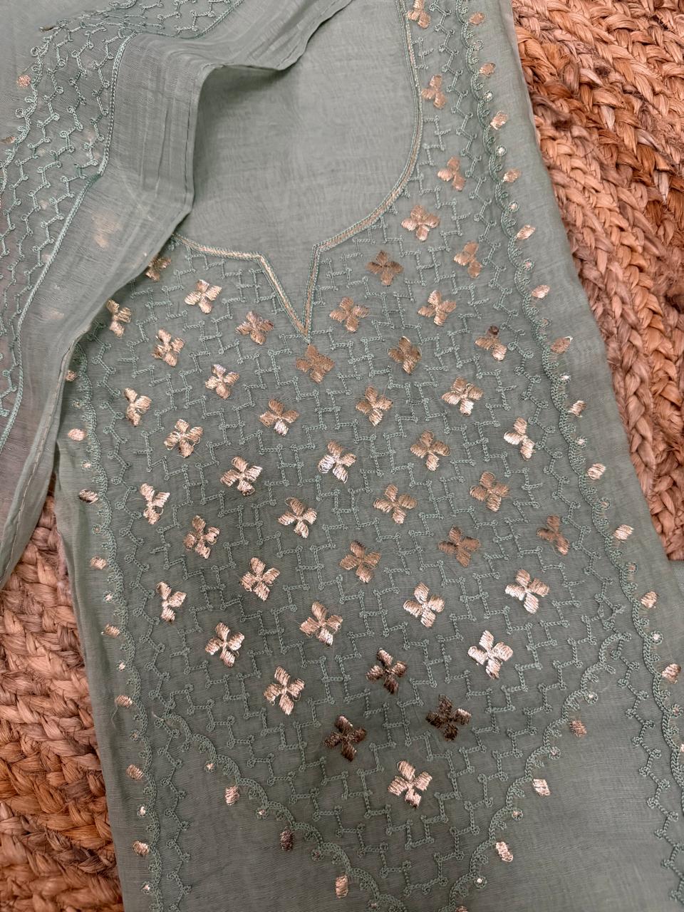 Powder green Chanderi silk kurta fabric – close-up of V-neckline with dense gold pita work floral butti motifs and silver sequin lattice on rattan surface