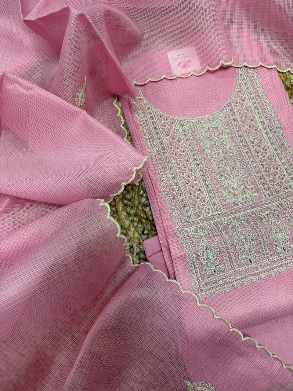 Powder pink Kota weave suit set – angled flat lay on rattan surface showing round neckline kurta with sage green dori embroidery panel and scallop dupatta