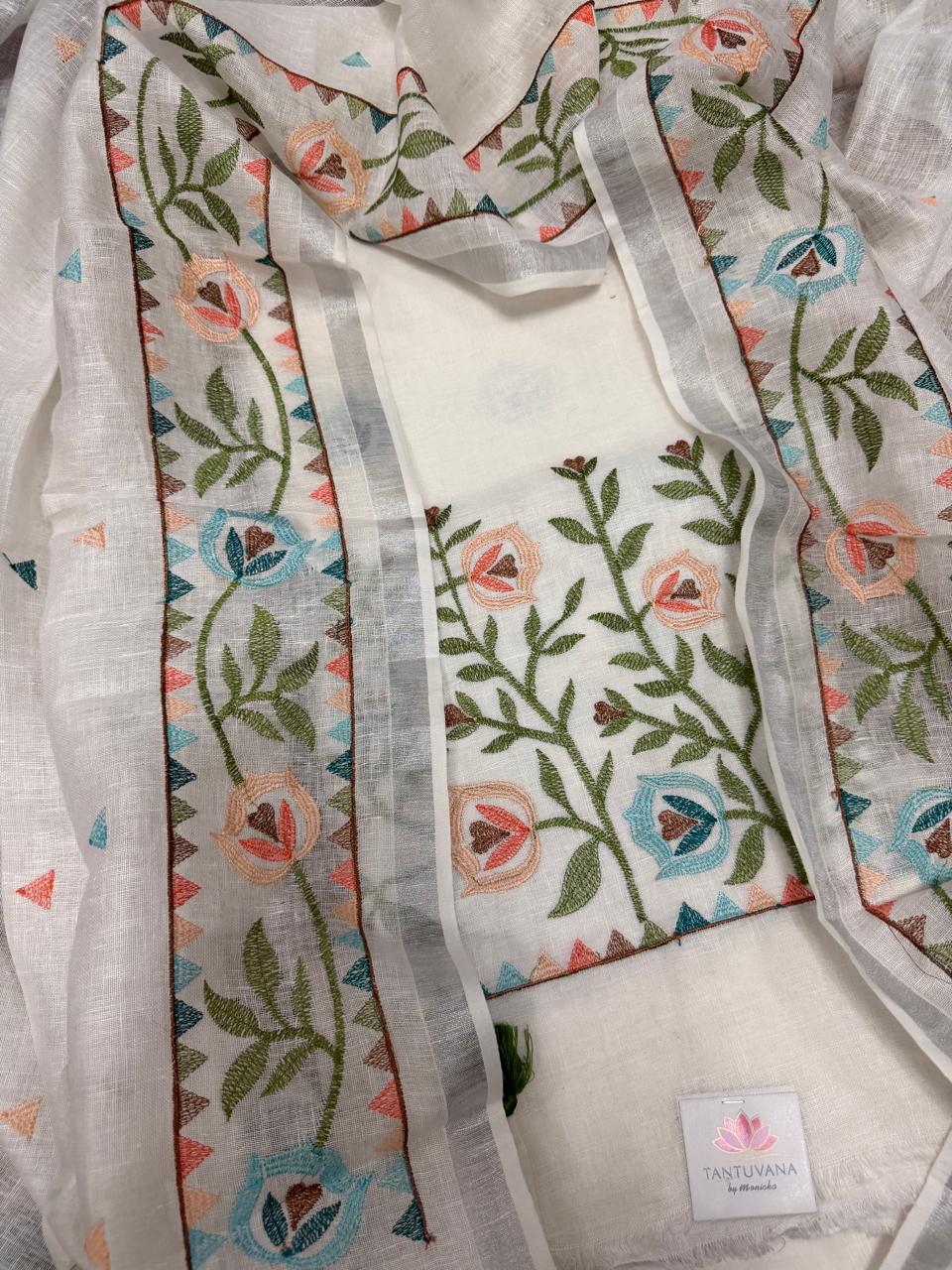 White linen 3-piece unstitched suit set – overhead flat lay showing kurta with dense multicolour floral vine machine embroidery and dupatta with geometric border