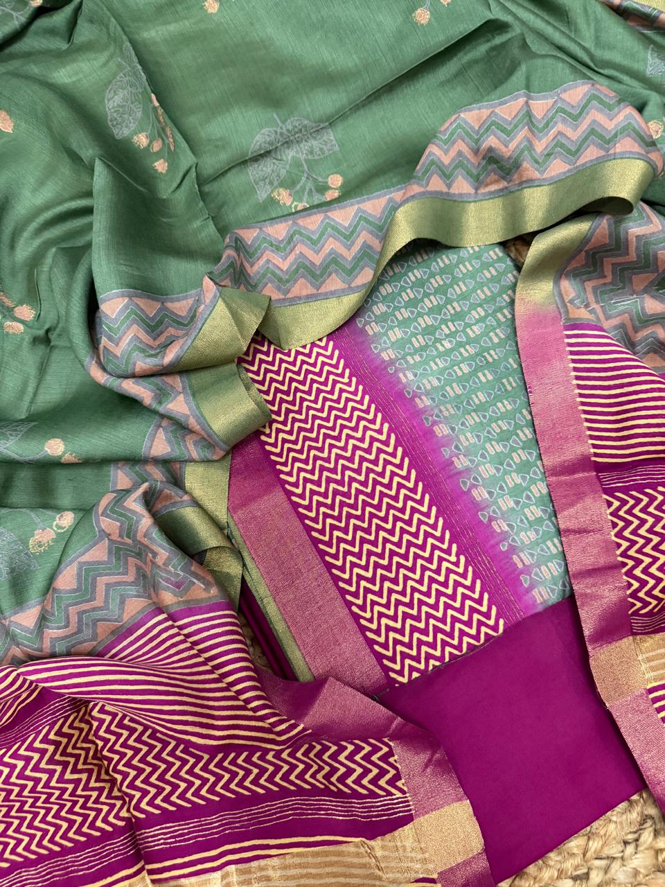 Light forest green and purple Maheshwari silk 3-piece unstitched suit set – draped flat lay showing forest green kurta with floral butti, pink chevron dupatta border with gold zari, and purple chevron bottom fabric