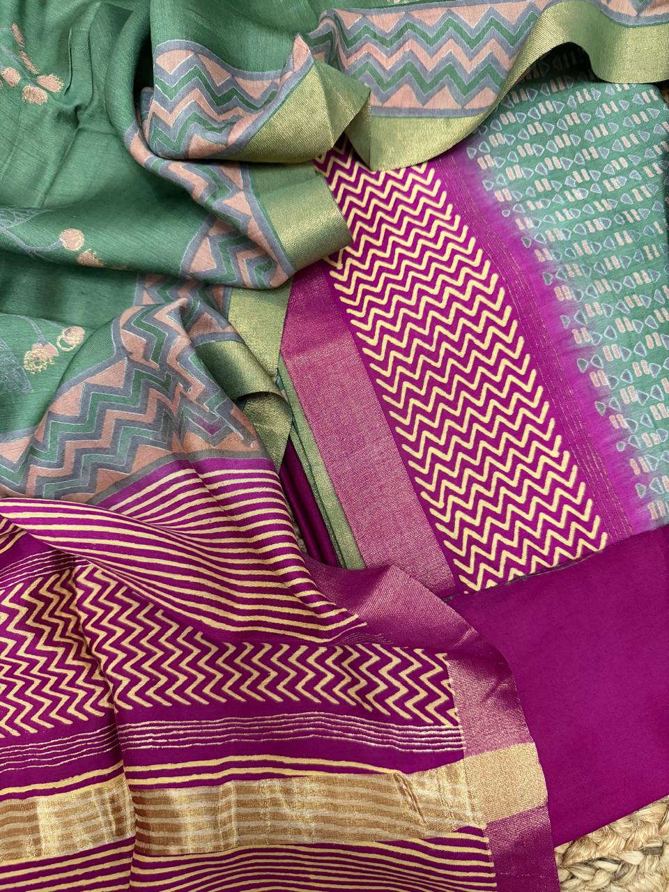 Light forest green and purple Maheshwari silk suit set – angled flat lay showing forest green kurta with floral butti, purple bottom with gold chevron zari border, and pink-green dupatta chevron border detail