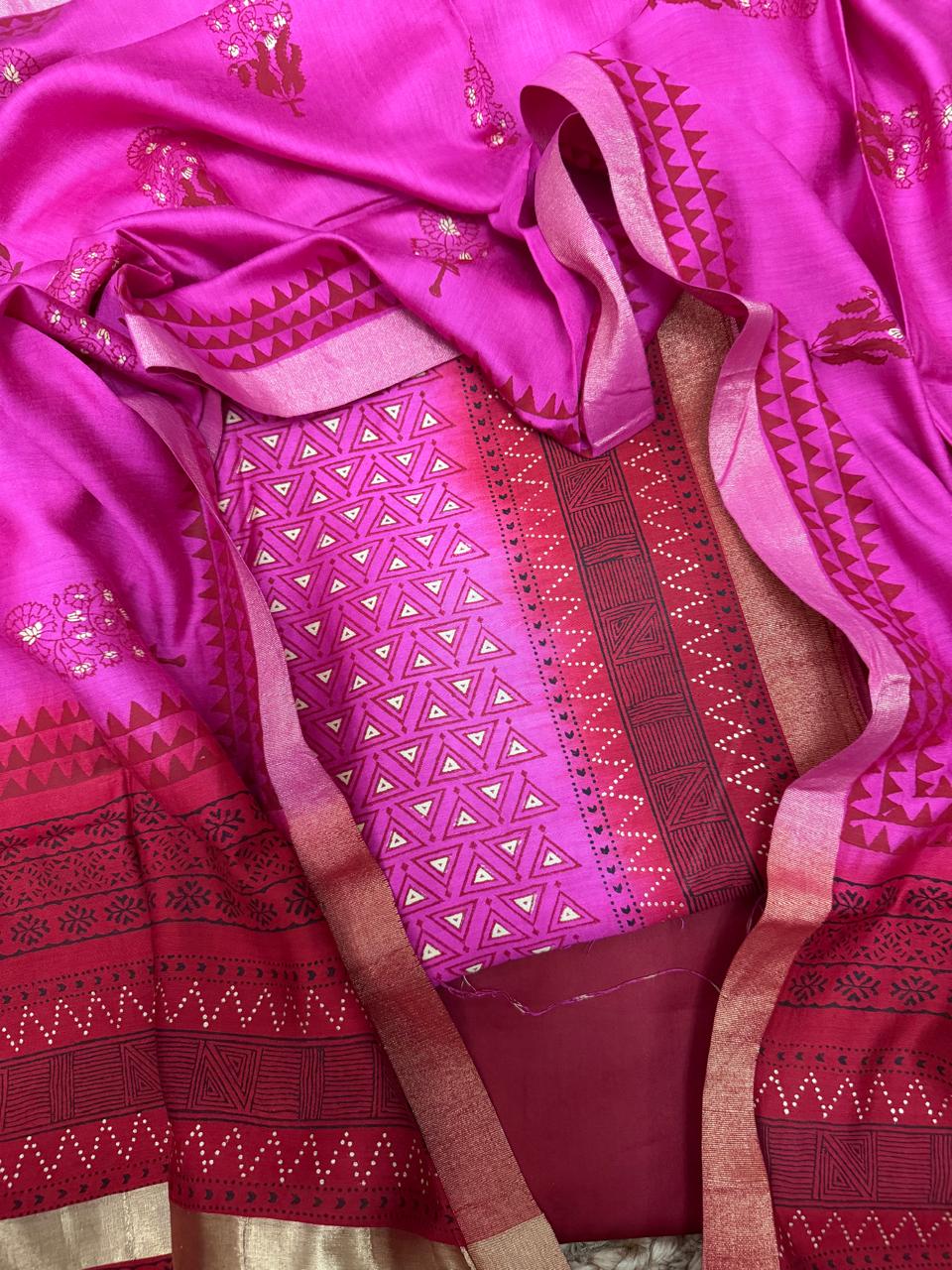 Pink and red Maheshwari silk 3-piece unstitched suit set – overhead flat lay showing pink triangle geometric khari print kurta, red cotton silk bottom with maze block print and bandhani dot border, and fuchsia silk dupatta with floral butti and gold zari border