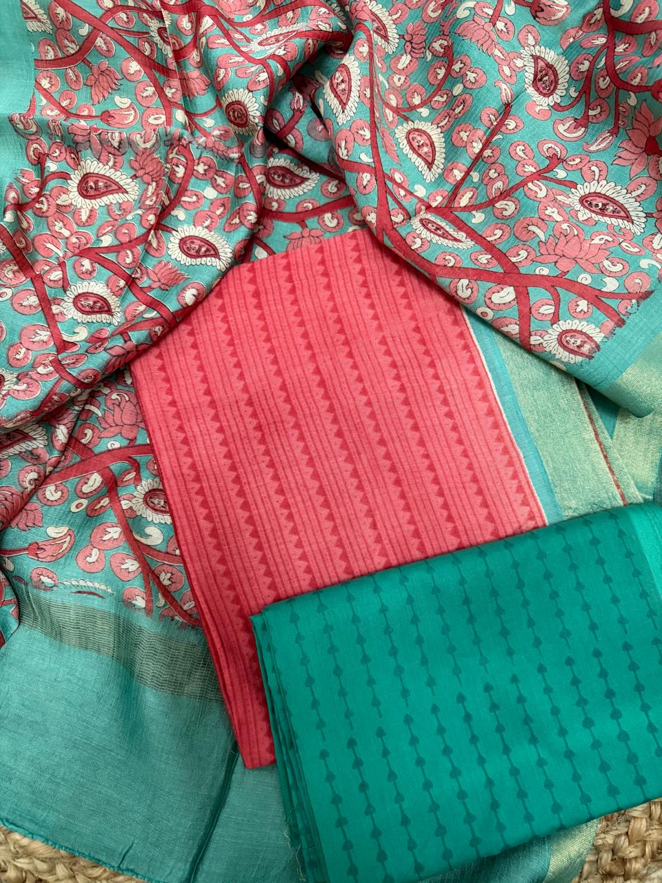 Teal and coral Maheshwari silk 3-piece unstitched suit set – overhead flat lay on rattan showing coral stripe zigzag kurta, teal dot-chain cotton bottom, and teal Kalamkari dupatta with pink lotus and paisley vine print, gold zari border