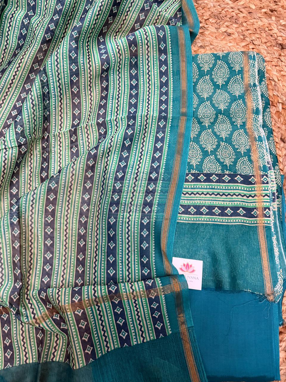 Teal and navy Chanderi silk 3-piece unstitched suit set – angled flat lay on rattan showing navy-green geometric stripe and diamond booti dupatta with gold zari border alongside teal kurta with white paisley booti, navy diamond band, and plain teal Chanderi bottom