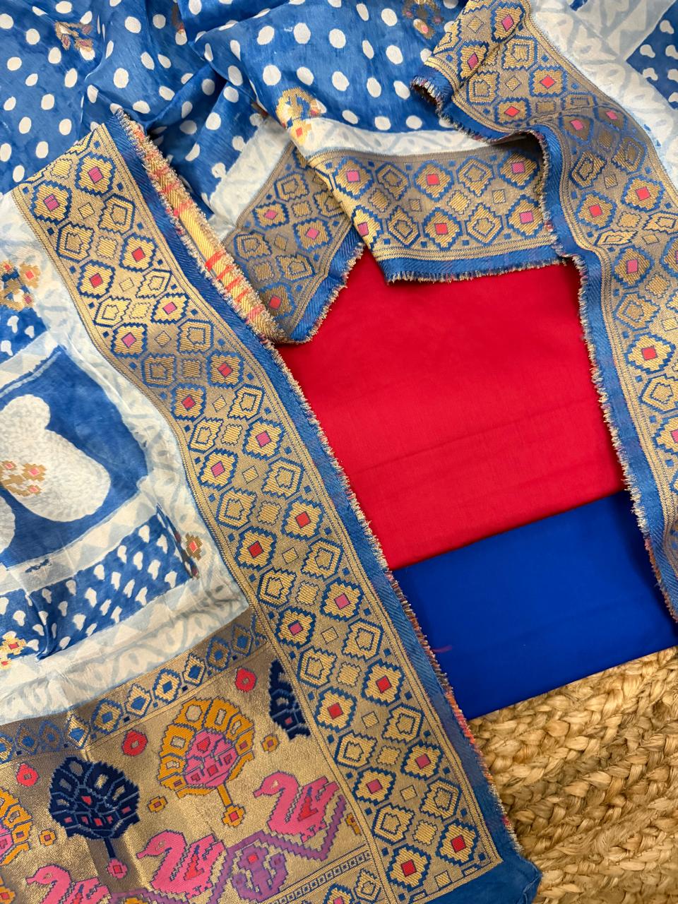 Fuchsia pink and royal blue 3-piece unstitched suit set – flat lay on rattan showing fuchsia glaze cotton kurta, royal blue bottom, brocade dupatta border with gold zari diamond geometric weave, and Patola-style swan and tree pallu